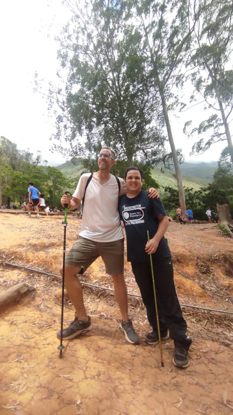 Dos senderistas con bastones juntos en la parte alta del cerro El Ávila después de completar la subida, con Caracas al fondo