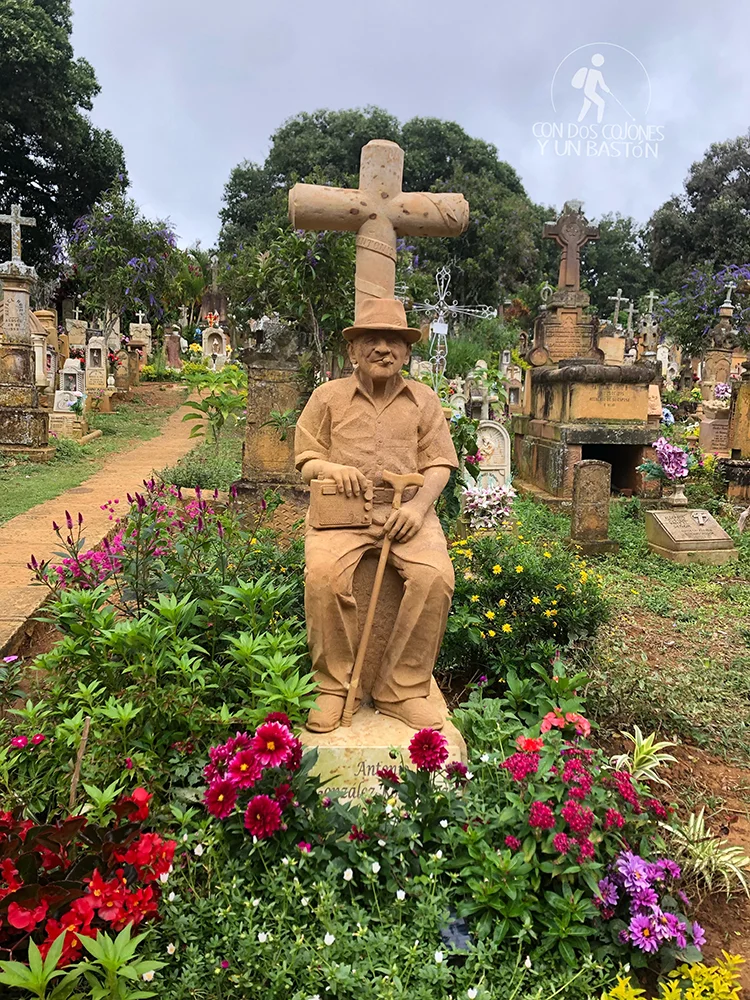 Escultura funeraria tallada en piedra entre tumbas y flores del cementerio de Barichara
