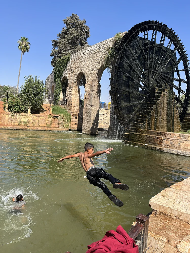 Niños jugando junto al río Orontes y las históricas norias de Hama, Siria