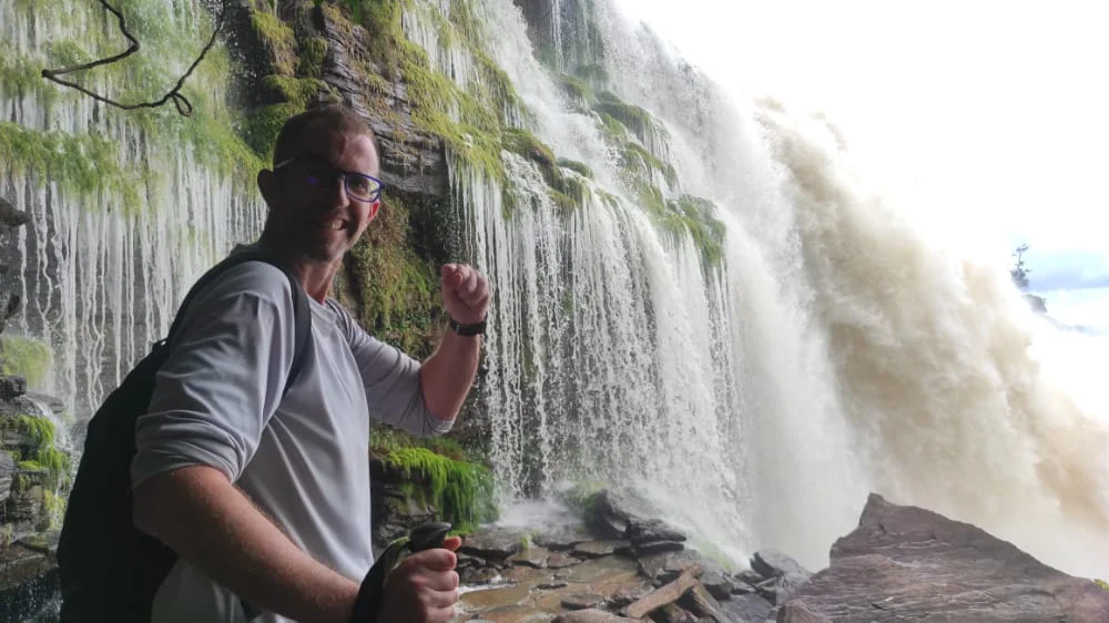 Viajero con discapacidad visual junto a una cascada durante su recorrido por Canaima